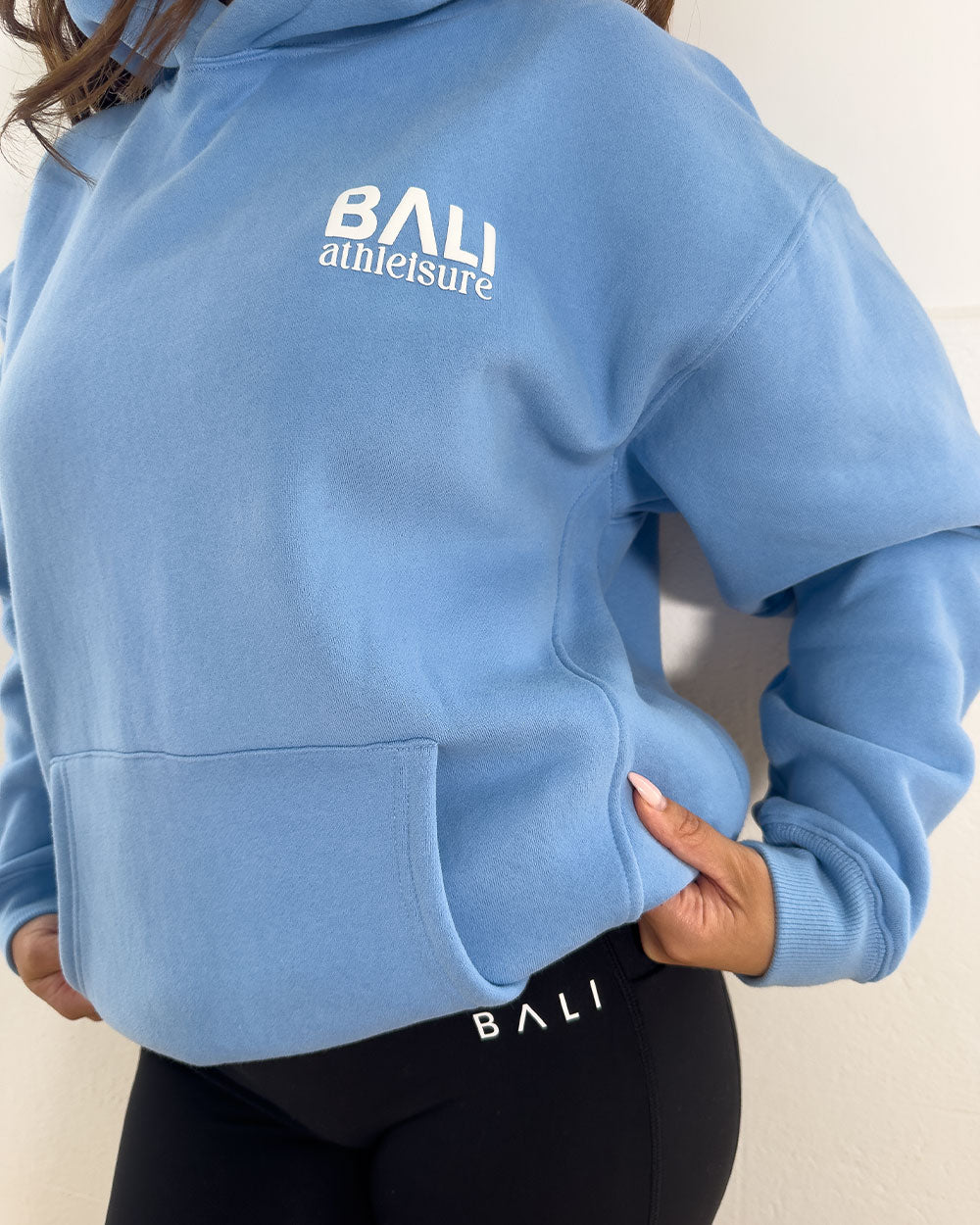 Person wearing a blue hoodie with 'Bali Athleisure' branding on a neutral background