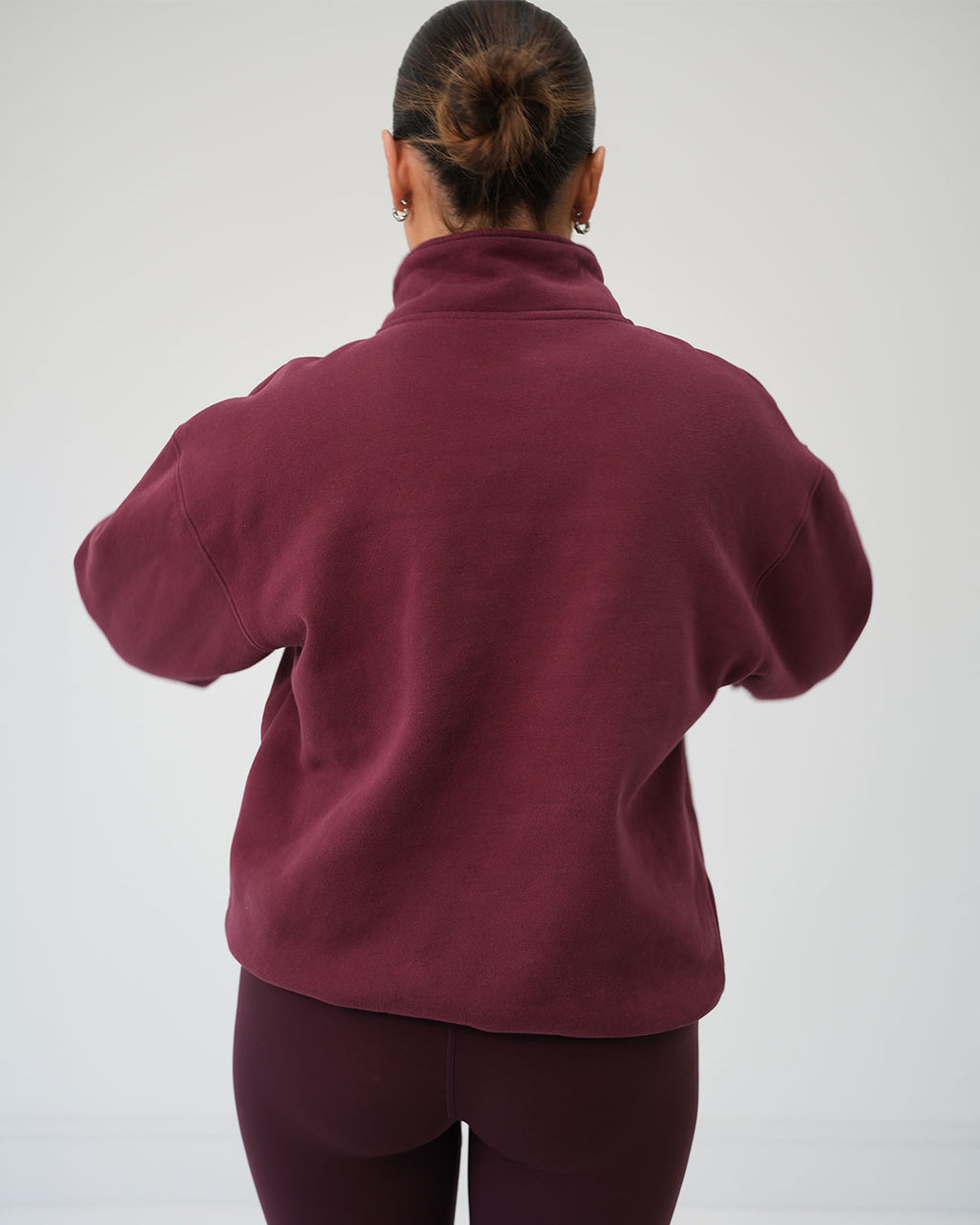 BALI luxury half-zip pullover styled for morning school runs and casual walks. A woman viewed from behind wearing a dark burgundy fleece pullover and matching leggings against a plain light grey studio background.
