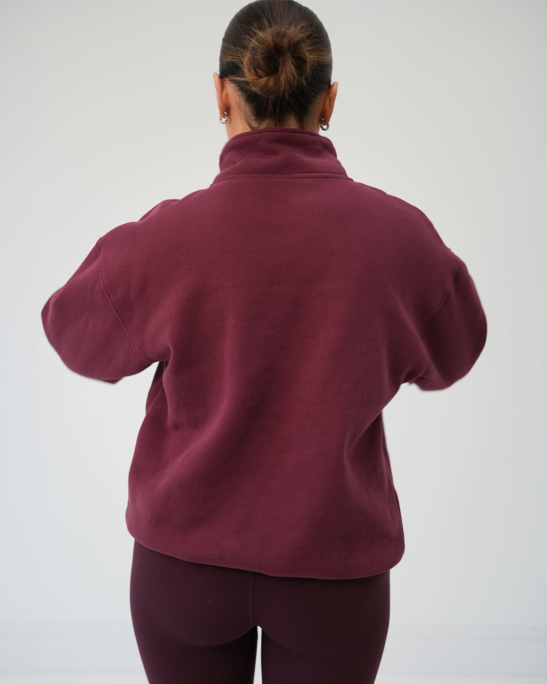  BALI luxury half-zip pullover styled for morning school runs and casual walks. A woman viewed from behind wearing a dark burgundy fleece pullover and matching leggings against a plain light grey studio background.