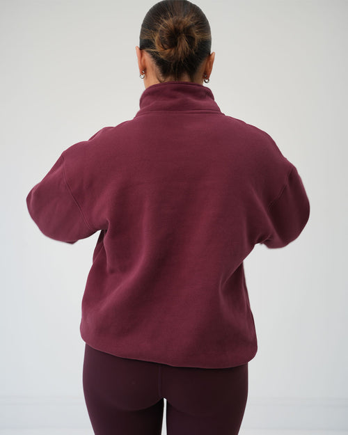  BALI luxury half-zip pullover styled for morning school runs and casual walks. A woman viewed from behind wearing a dark burgundy fleece pullover and matching leggings against a plain light grey studio background.