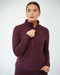 A woman modeling a dark plum purple athletic BALI zip-up jacket with a high collar and subtle tonal branding, set against a plain light gray studio background.